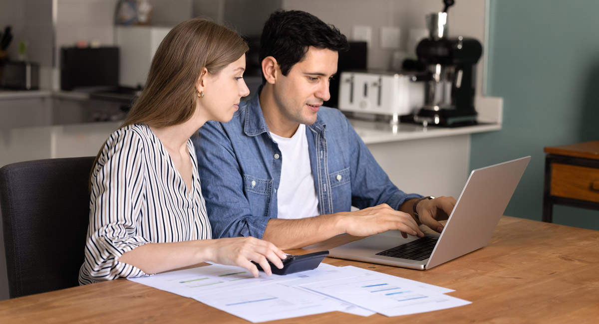 Couple using laptop and calculator at kitchen table