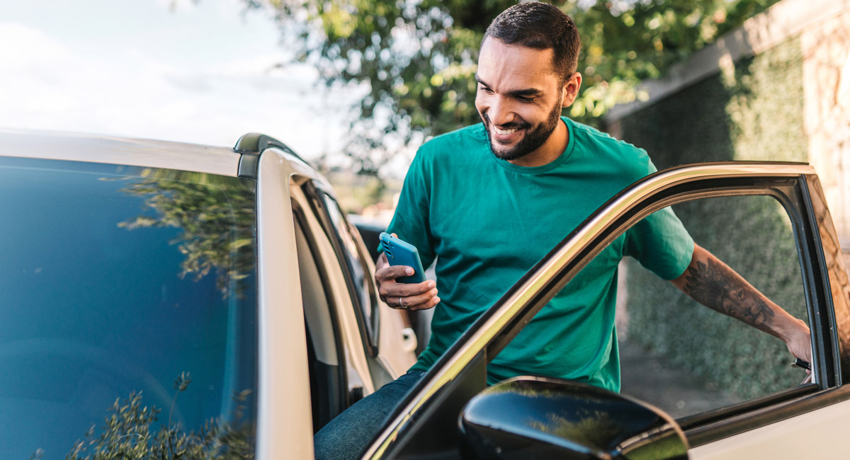 Man getting out of car while looking at phone and smiling