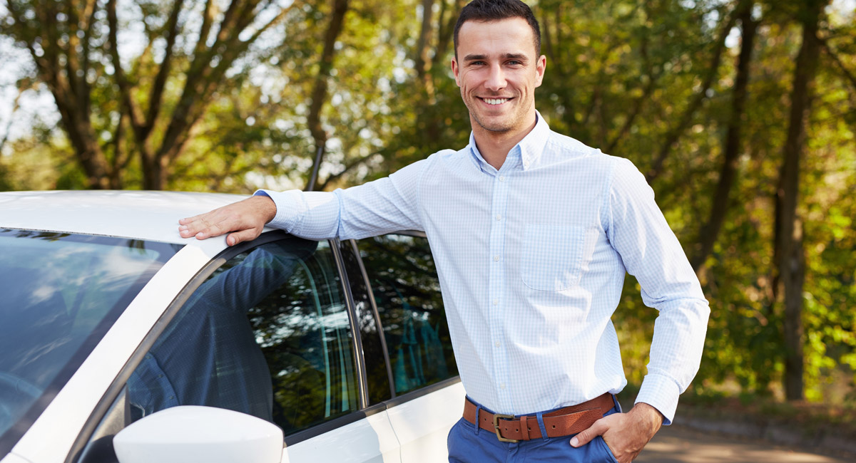 Man leaning on car and smiling outdoors