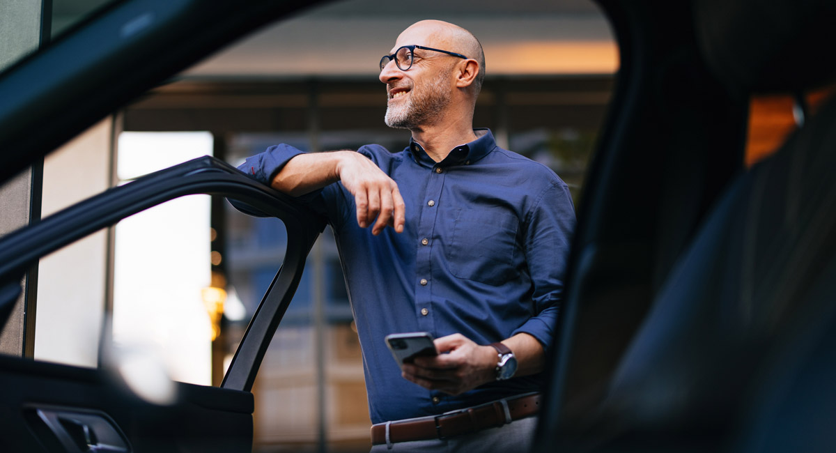 Man leaning on open car door holding phone