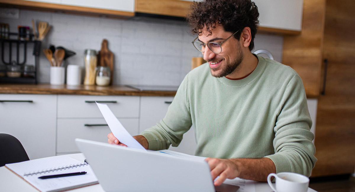 Man-reviewing-document-while-using-laptop-at-table