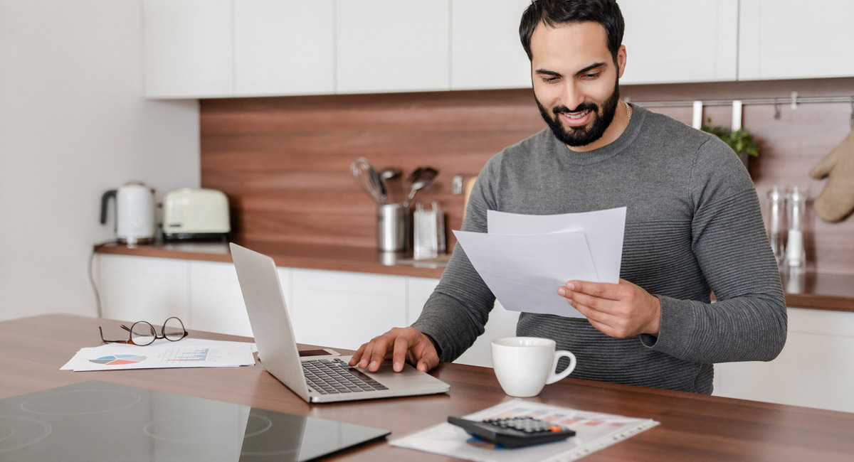 Man reviewing documents at kitchen table with laptop