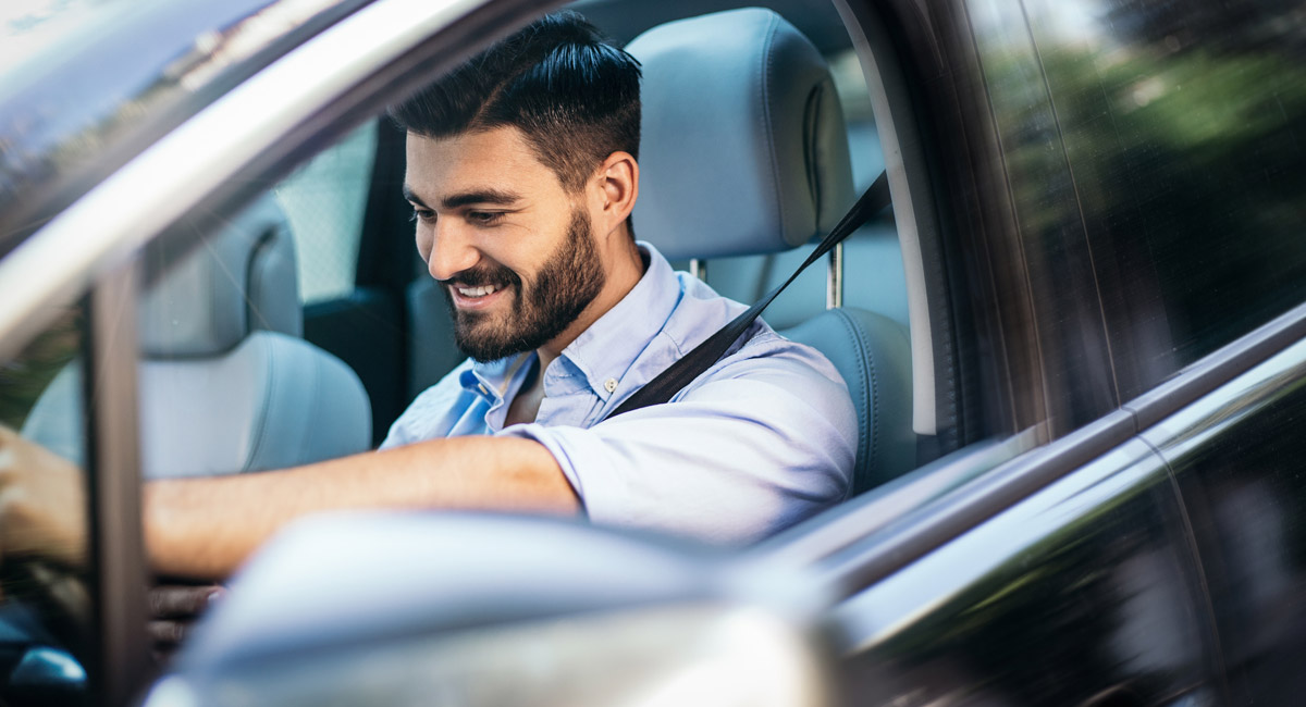 Man smiling while driving car and looking down