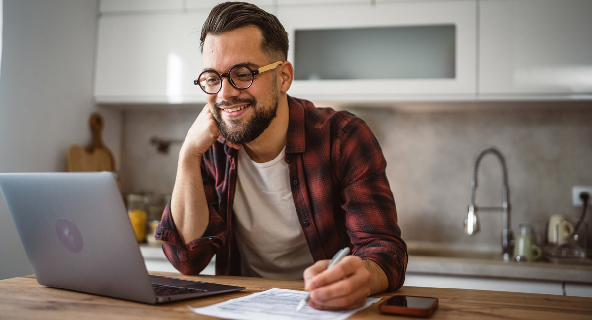 Man smiling while working on laptop and paperwork