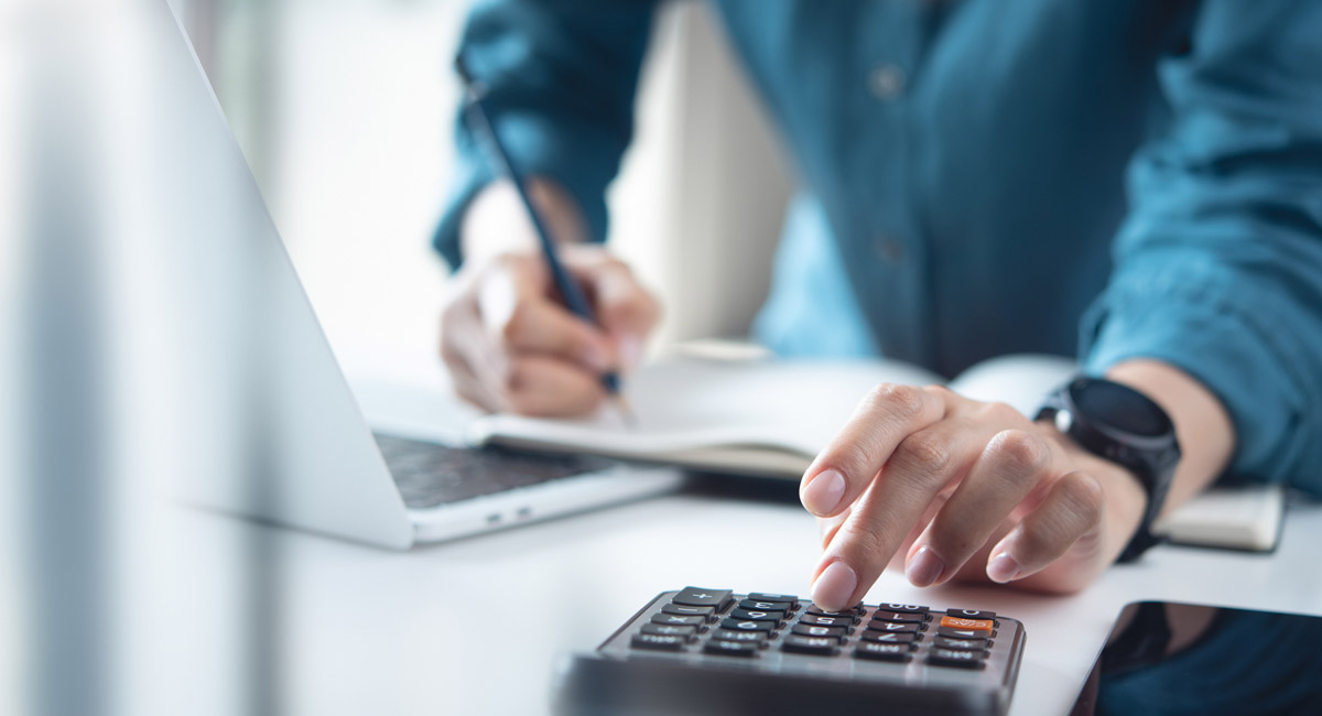 Person calculating expenses with calculator and laptop