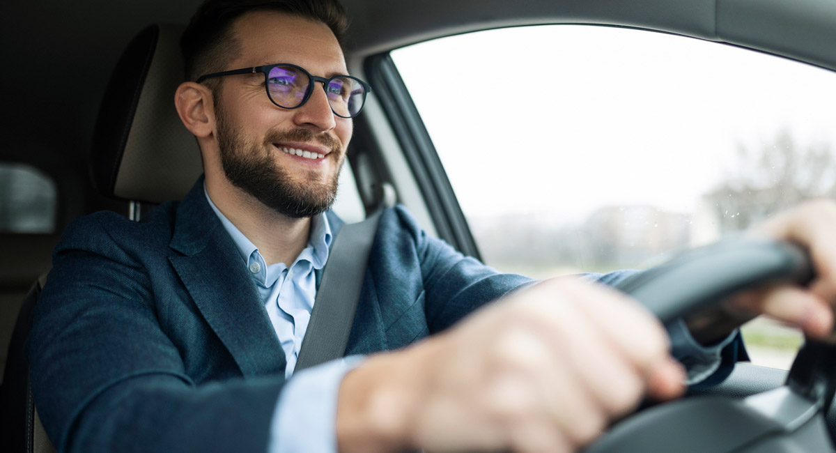 Smiling man driving car with hands on steering wheel
