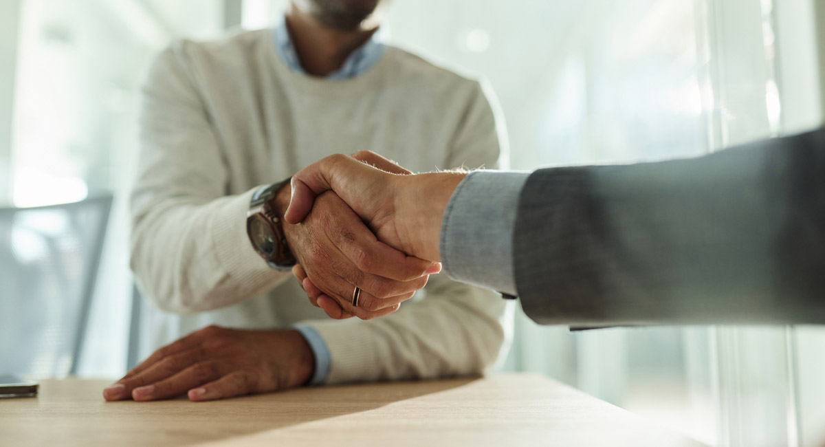 Two men shaking hands across a desk in office setting