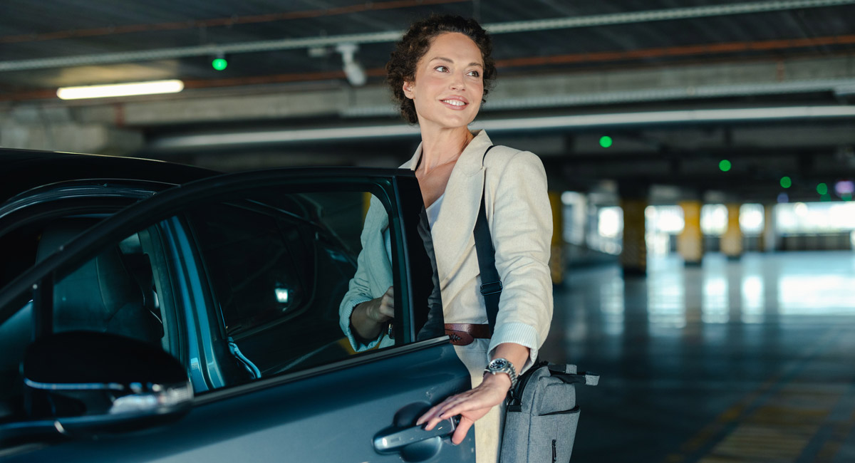 Woman opening car door in parking garage with bag