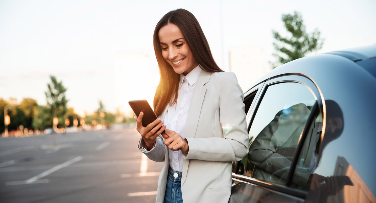 Woman standing by car using phone and smiling