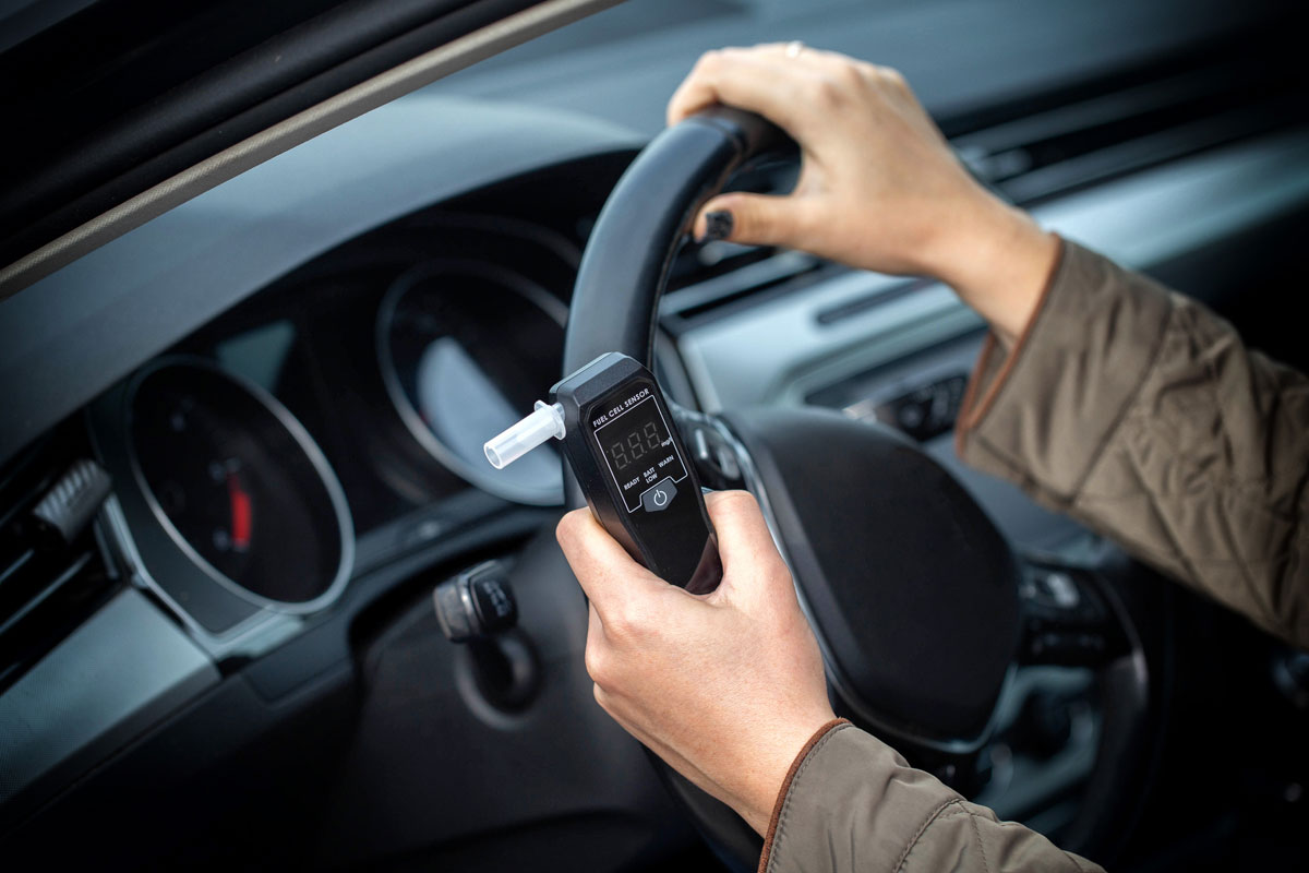 female-driver-with-one-hand-on-steering-wheel-and-the-other-holding-a-breathalyzer