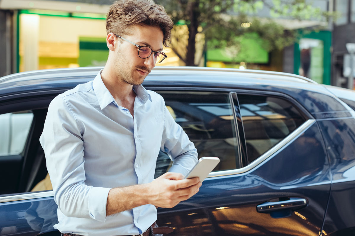 young-man-standing-next-to-blue-car-and-looking-down-at-phone