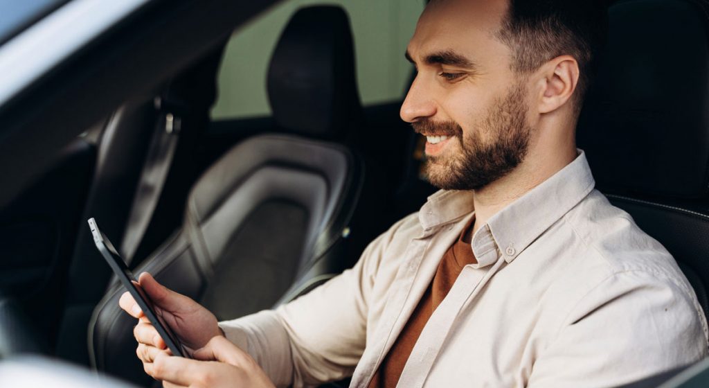 man-in-car-looking-at-phone-and-smiling