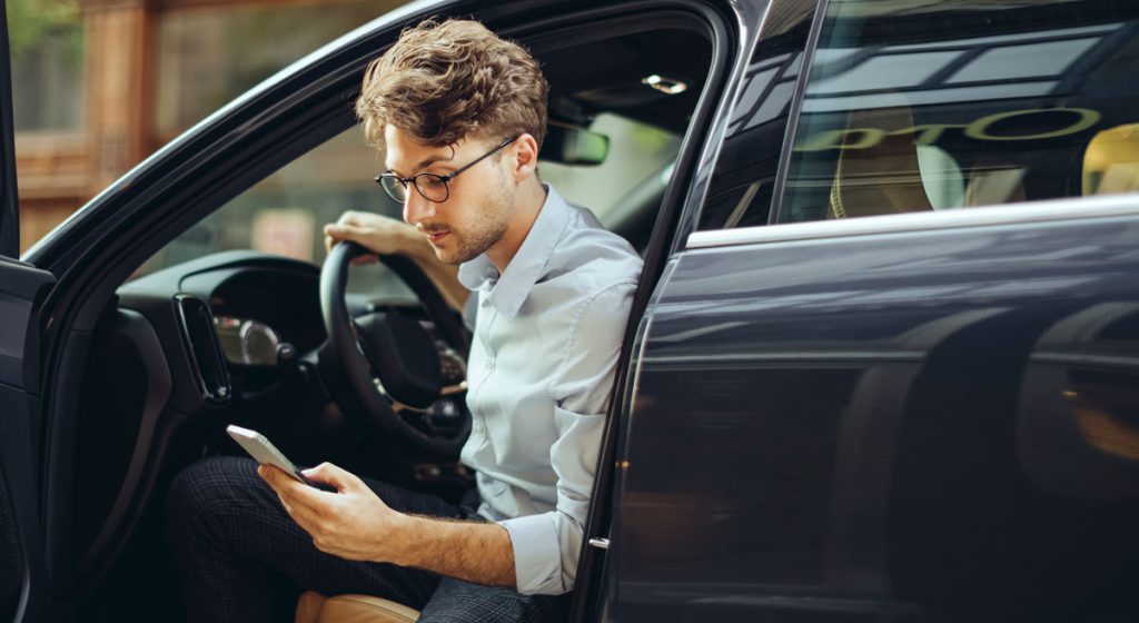 young-male-driver-exiting-driver's-seat-while-looking-down-at-phone