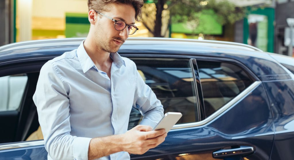 young-man-standing-next-to-blue-car-and-looking-down-at-phone